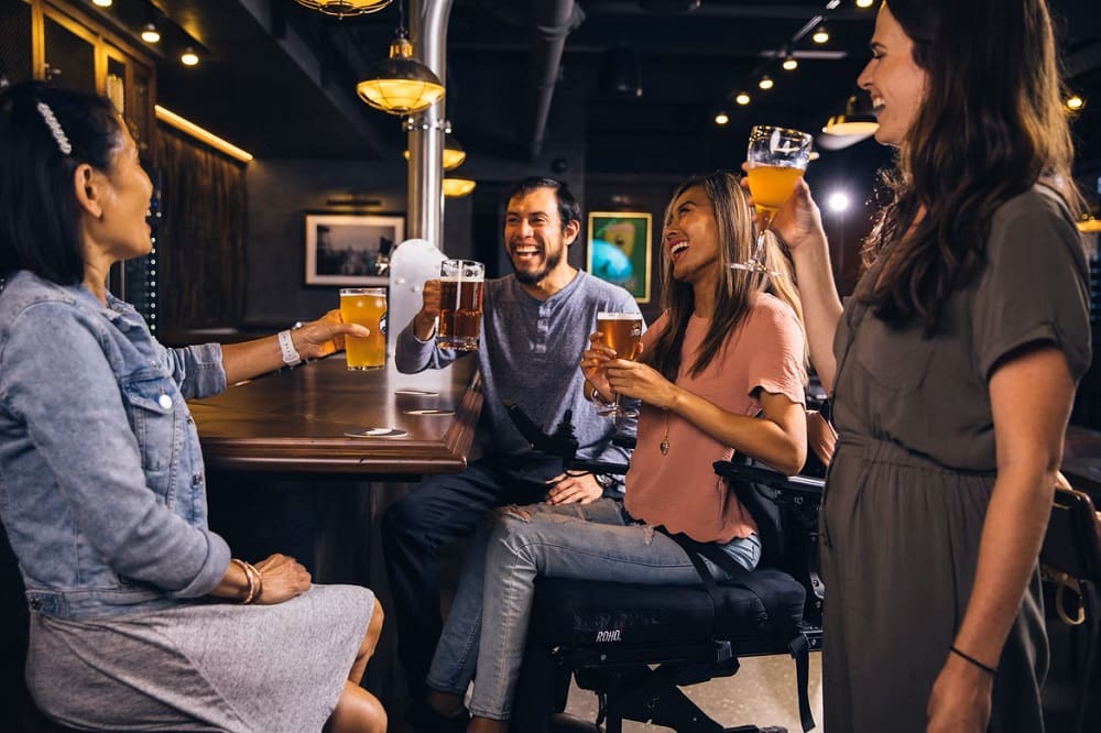 Group of smiling people sat around a bar with beers in hand