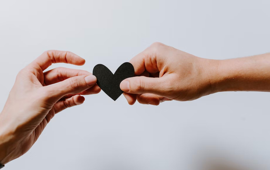 Two hands holding a black love heart cut out of paper