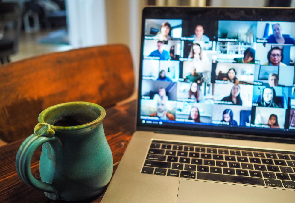 A blue mug on a wooden desk next to a laptop displaying an online meeting.