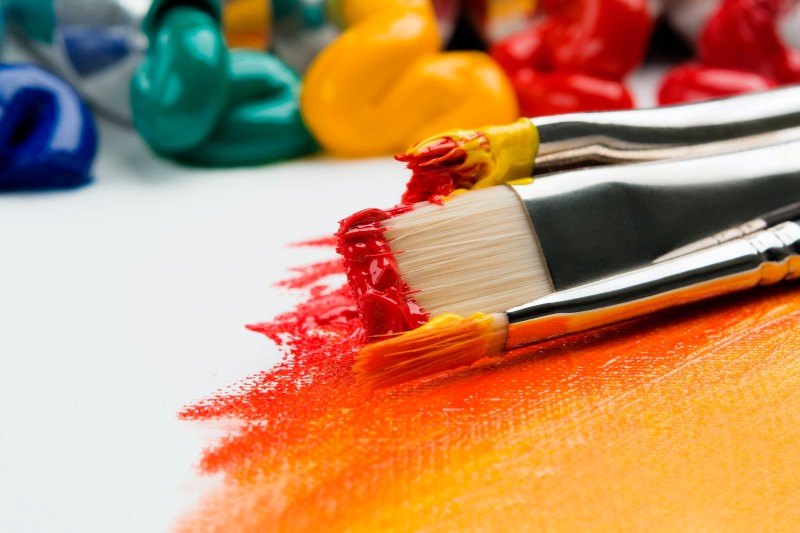 Two paintbrushes covered in red and yellow pain on canvas