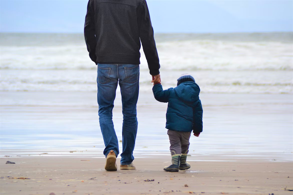 Adult and child holding hands walking on beach