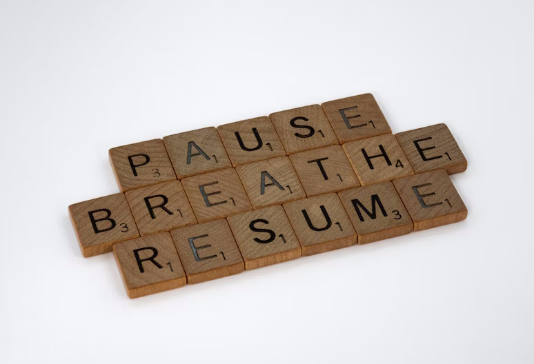 Wooden scrabble letters spelling out "pause", "breathe" and "resume".