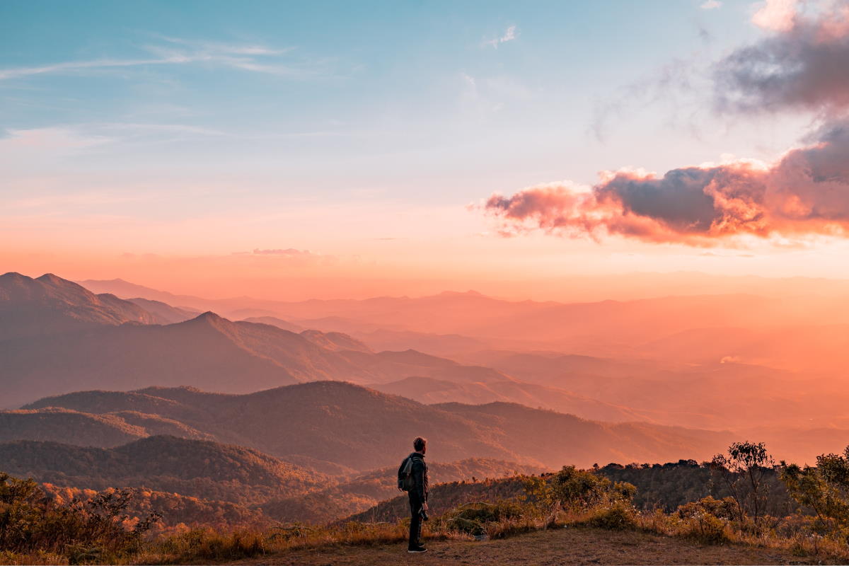 Person overlooking a mountainous landscape during sunset