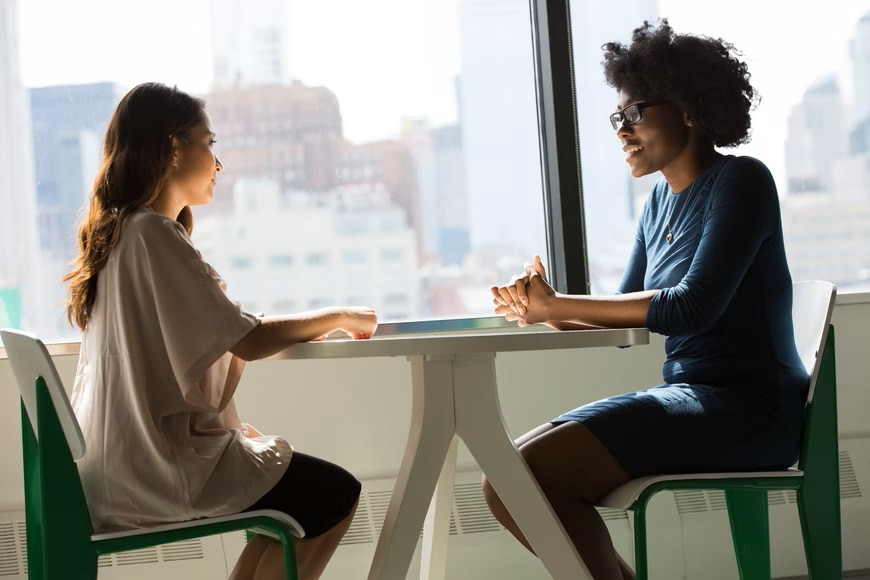 Two people sat opposite one another at table beside window