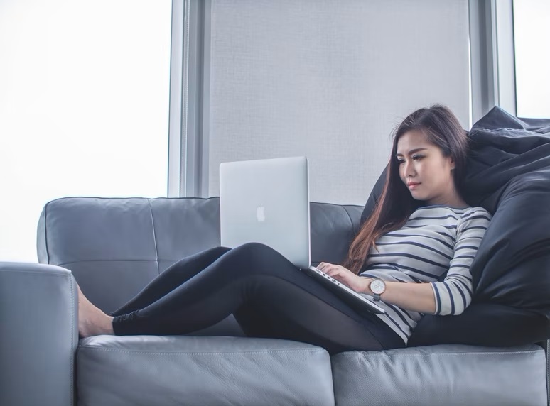 Woman in striped top lying on sofa and using laptop
