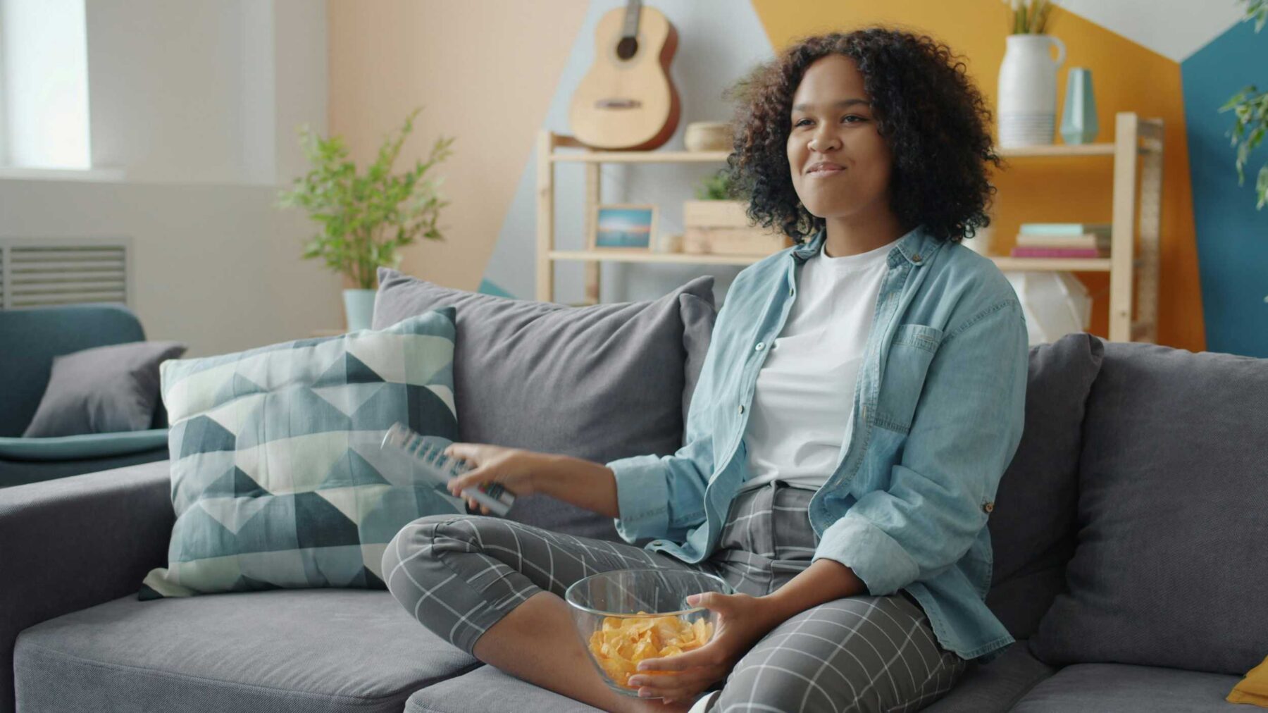 A woman sat cross-legged on a sofa, snacking.